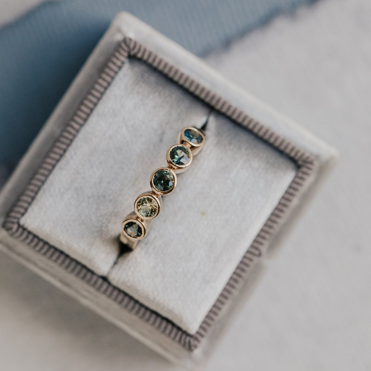 Gold ring with green and blue sapphires  in a jewelry box on a light background