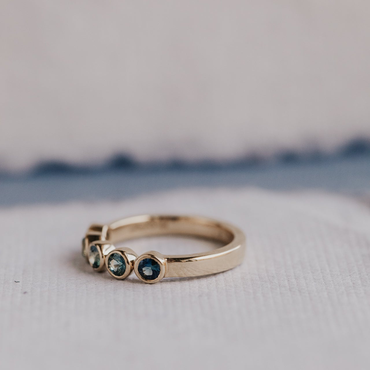 Gold ring with blue and green sapphires on a textured surface