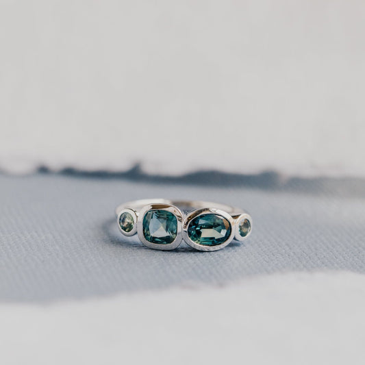 White gold ring with green and blue sapphires on a textured surface