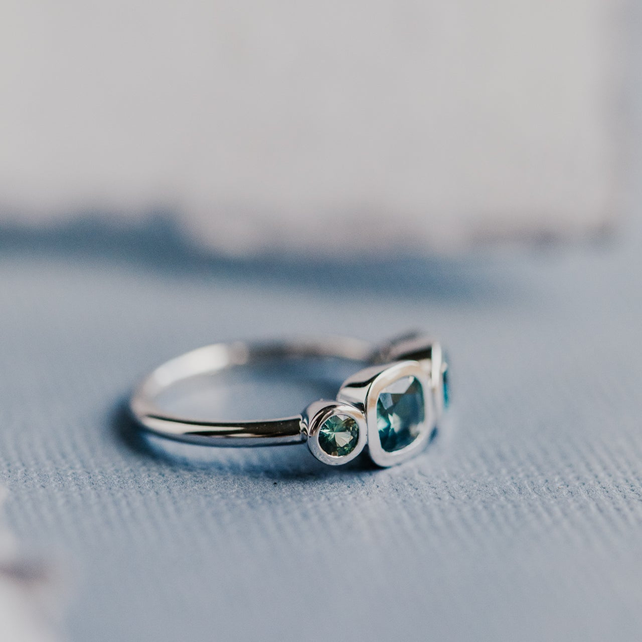 White gold ring with green sapphires on a textured surface