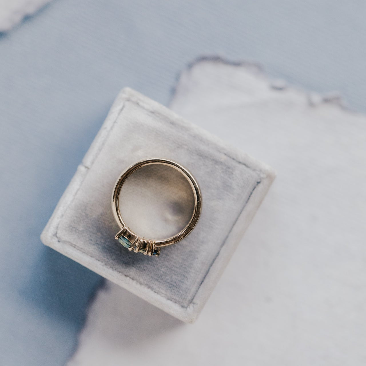 Gold ring on a white velvet cushion with a light blue background