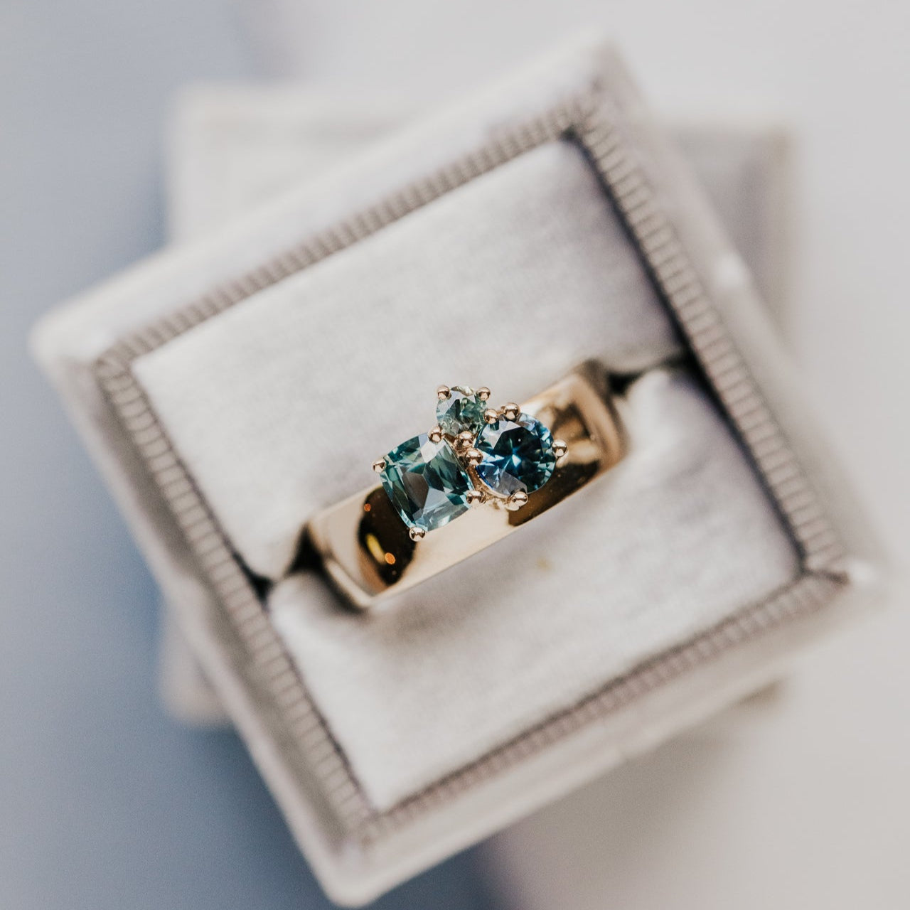 Gold ring with blue sapphires in a jewelry box on a light gray background