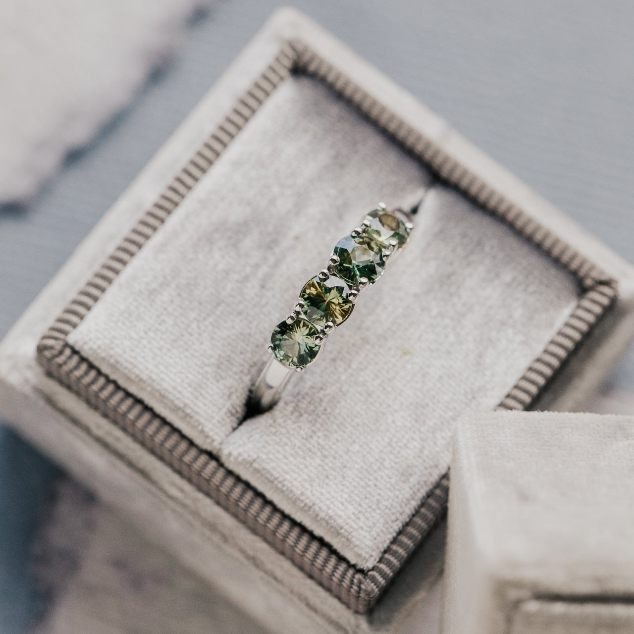 White gold ring with green and yellow sapphires on a textured gray surface