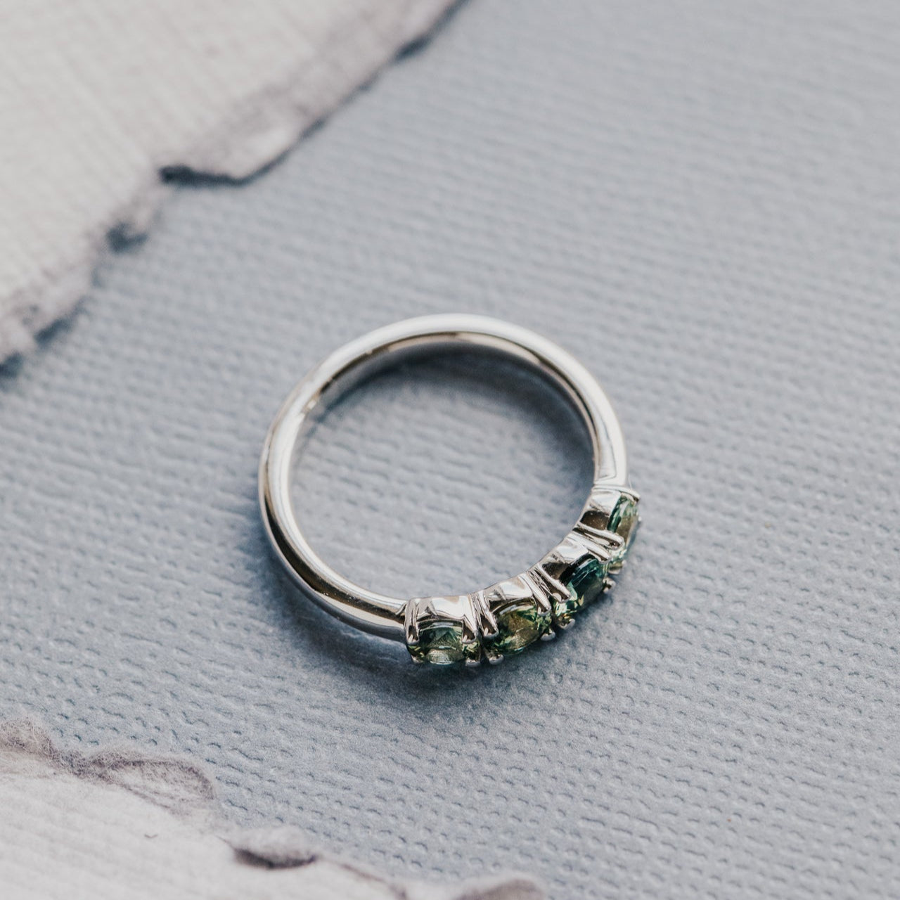 White gold ring with green and yellow sapphires on a textured gray surface