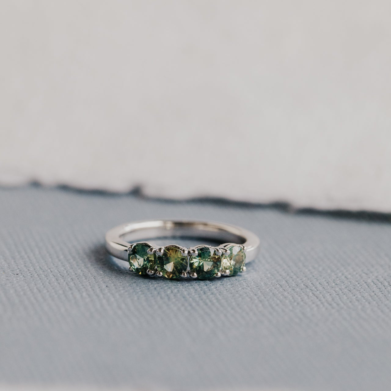 White gold ring with green and yellow  sapphire on a textured surface