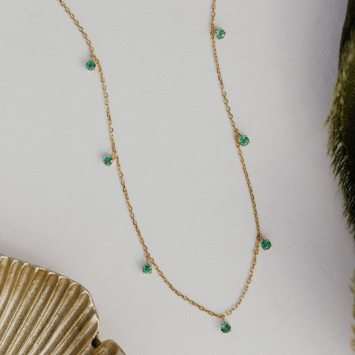 Gold necklace with green emerald gemstones on a white background.