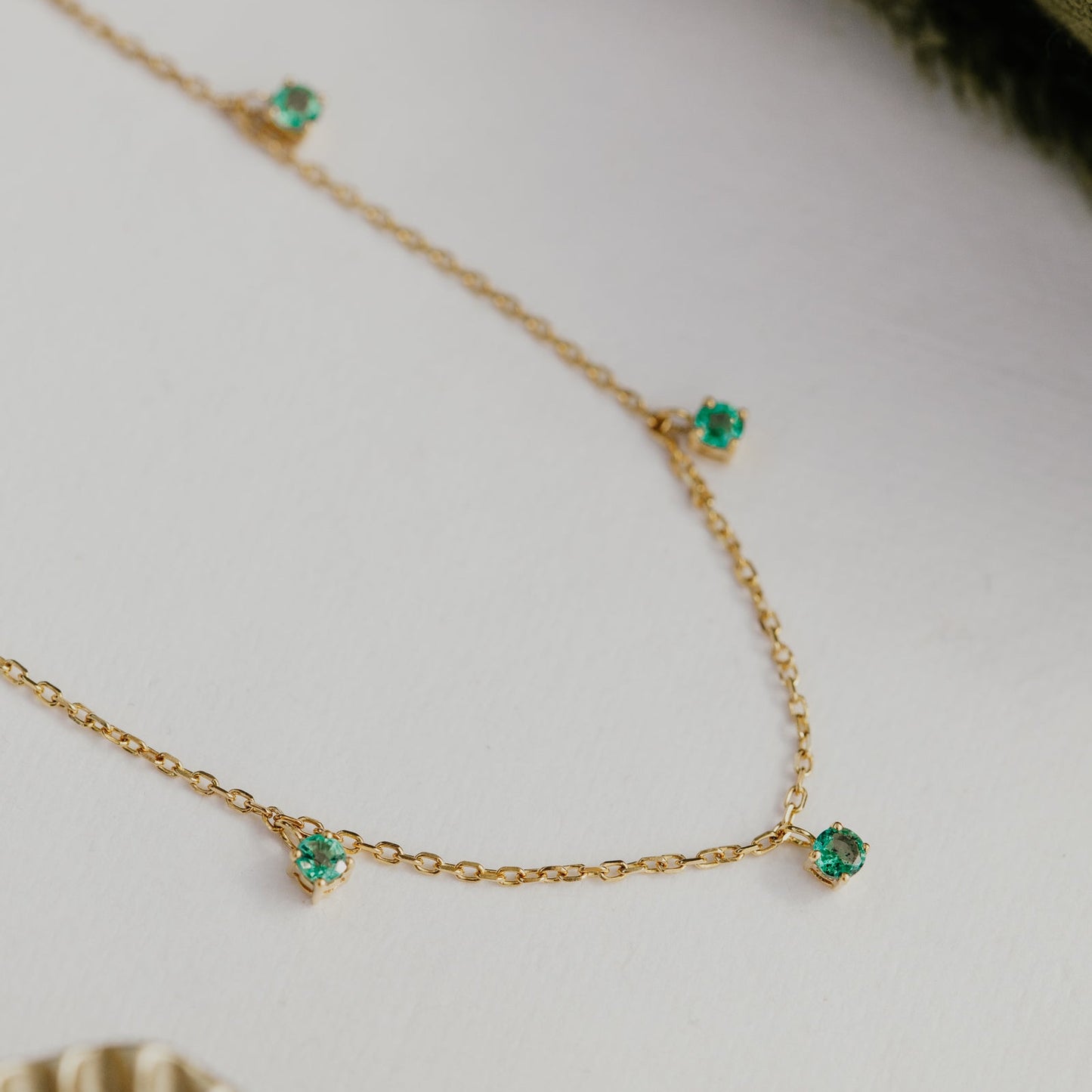 Gold necklace with emerald green emerald gemstones on a neutral background.