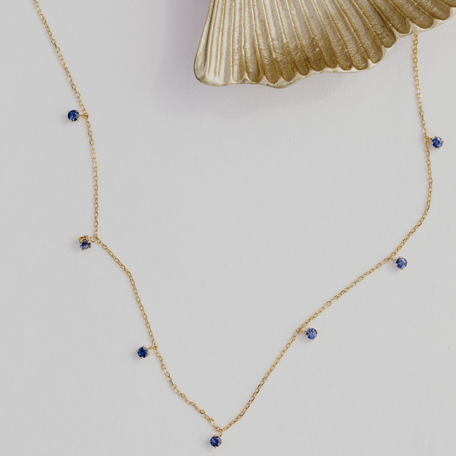 Gold necklace with blue seven sapphire dangles on a light gray background.