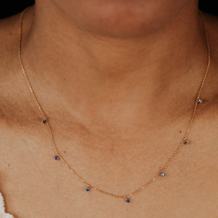 Gold necklace with seven blue sapphire stones on a person's neck.
