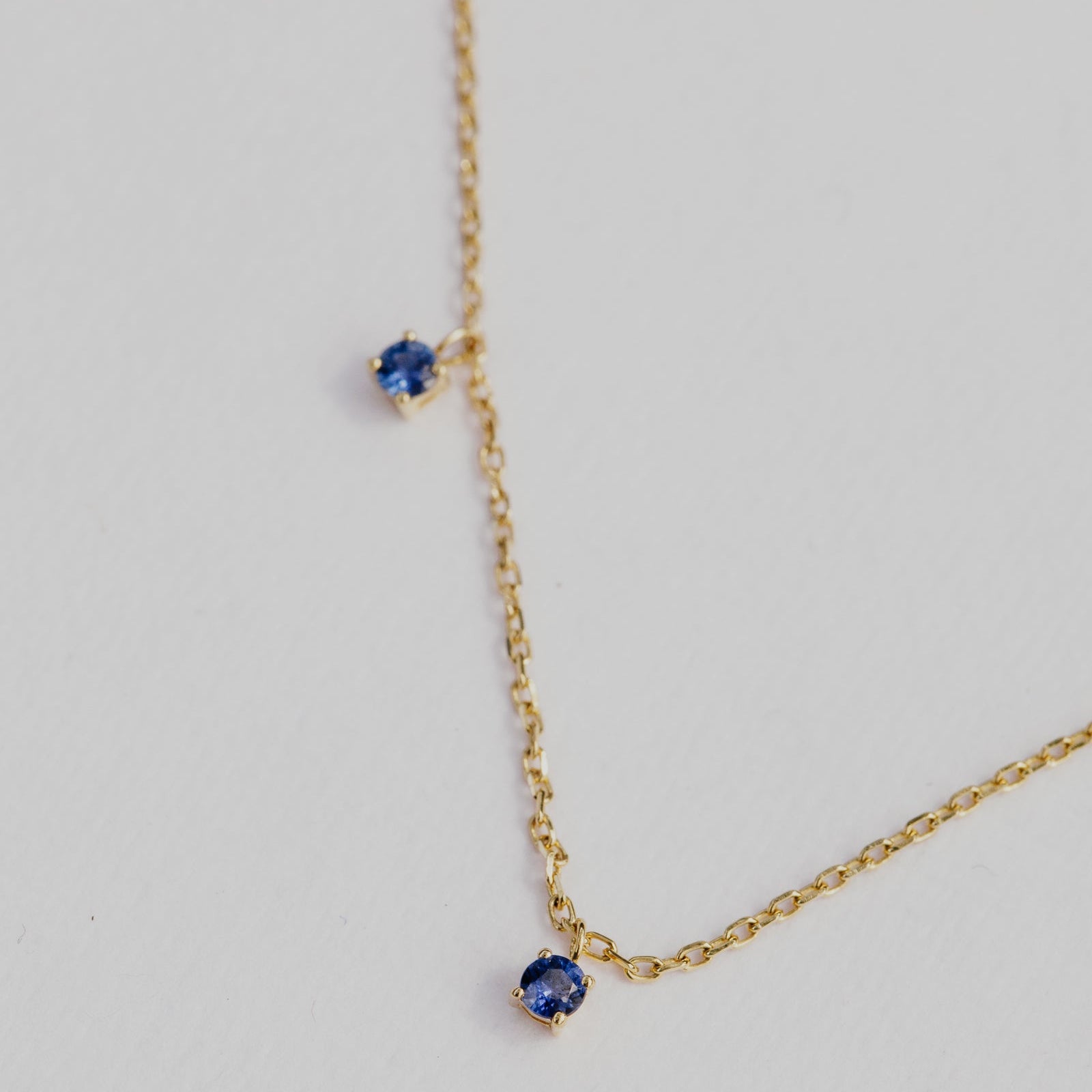 Gold necklace with blue sapphire gemstones on a light gray background.