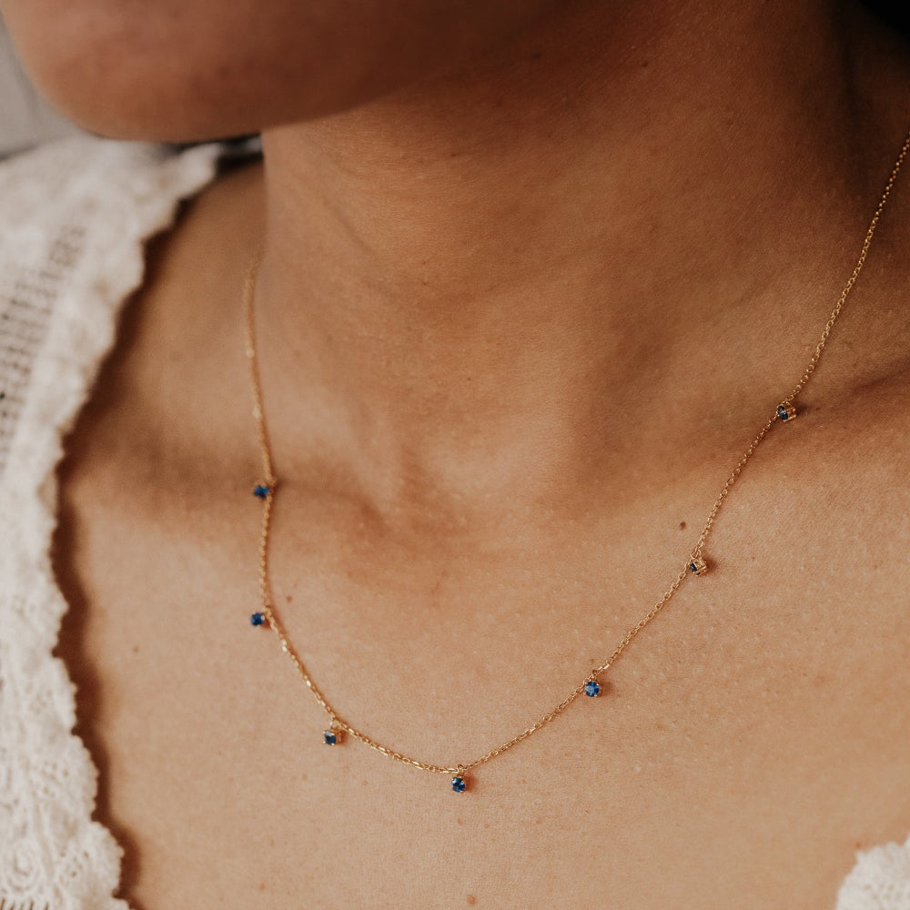 Necklace with small sapphires stones worn by a person.
