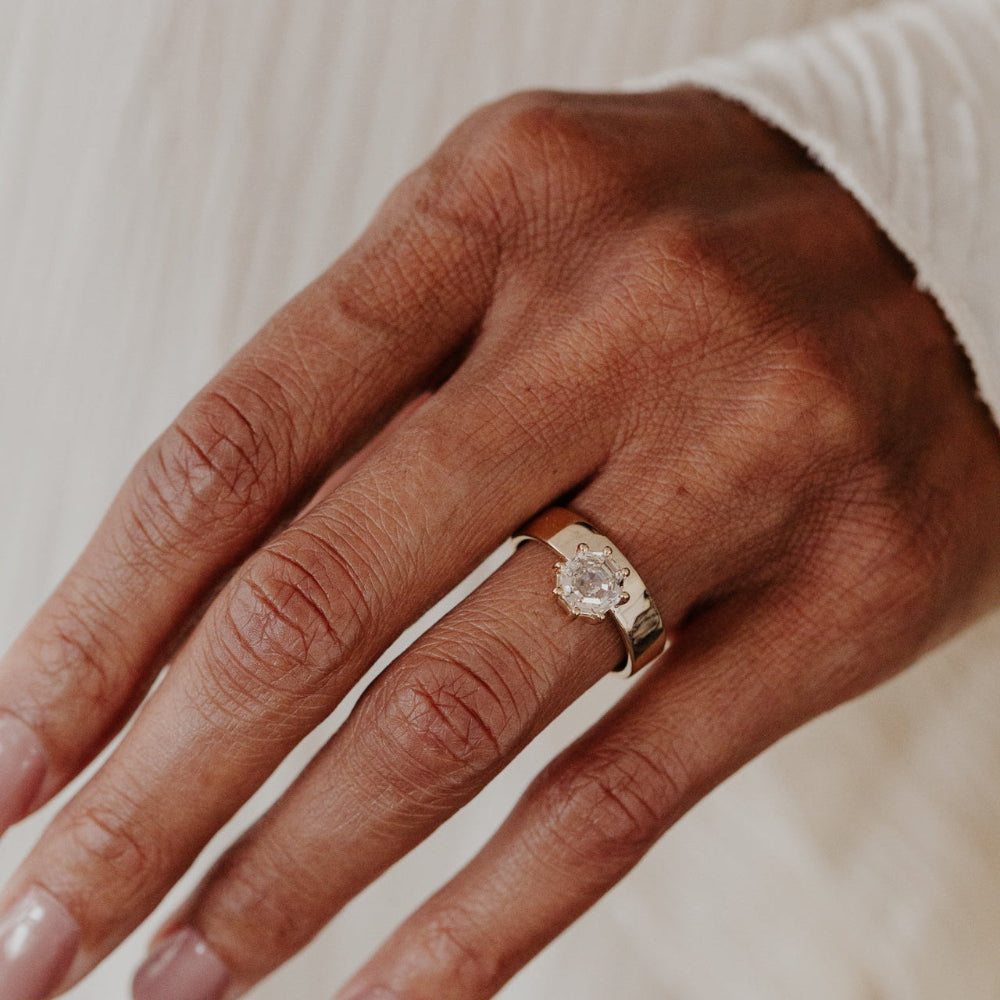 Hand wearing a gold ring with a octagon champagne diamond on a neutral background.