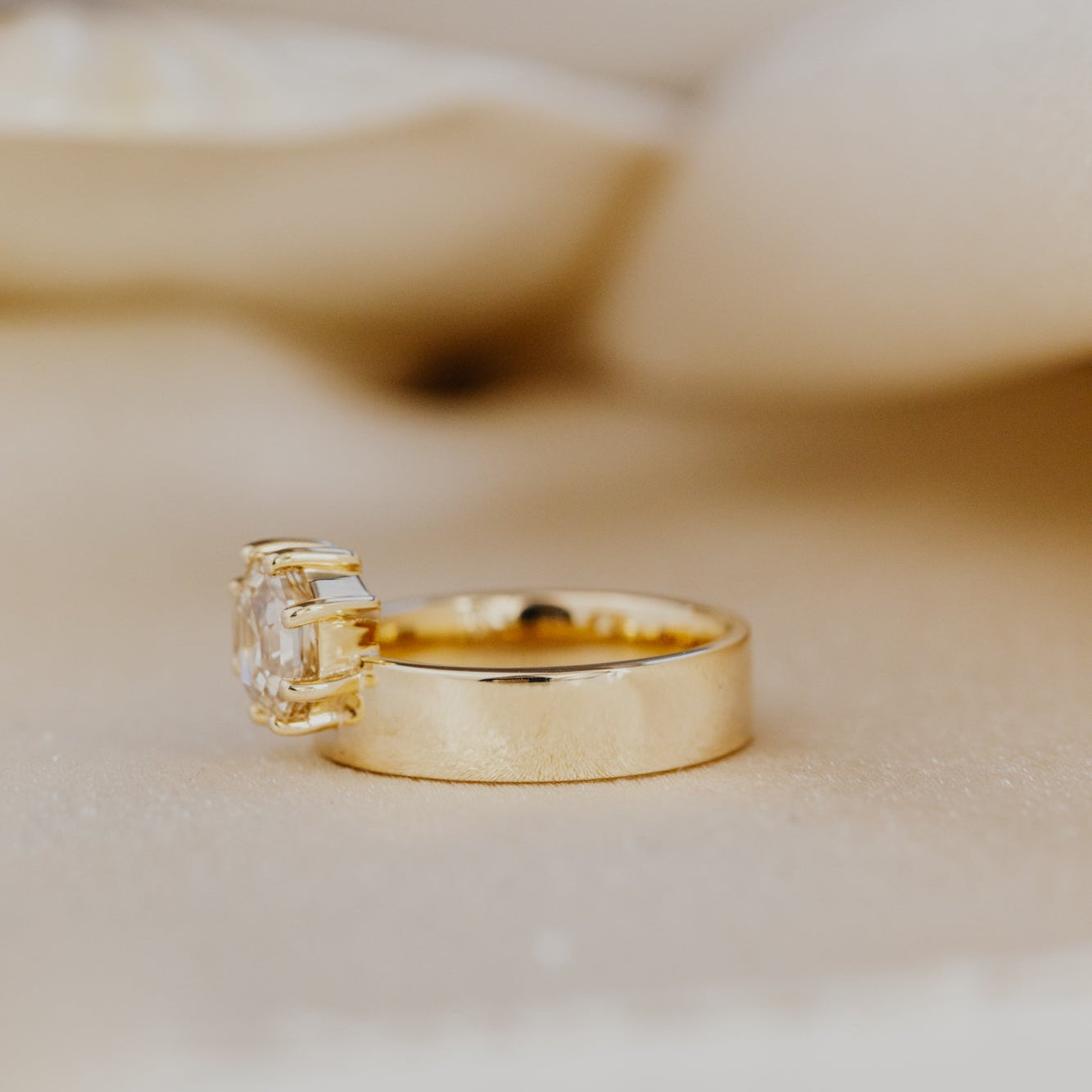 Gold engagement ring with a octagon champagne diamond on a beige background.