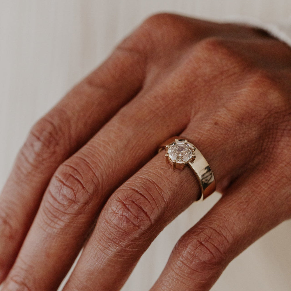 Close-up of a hand wearing a gold engagement  ring with a champagne diamond on a neutral background.