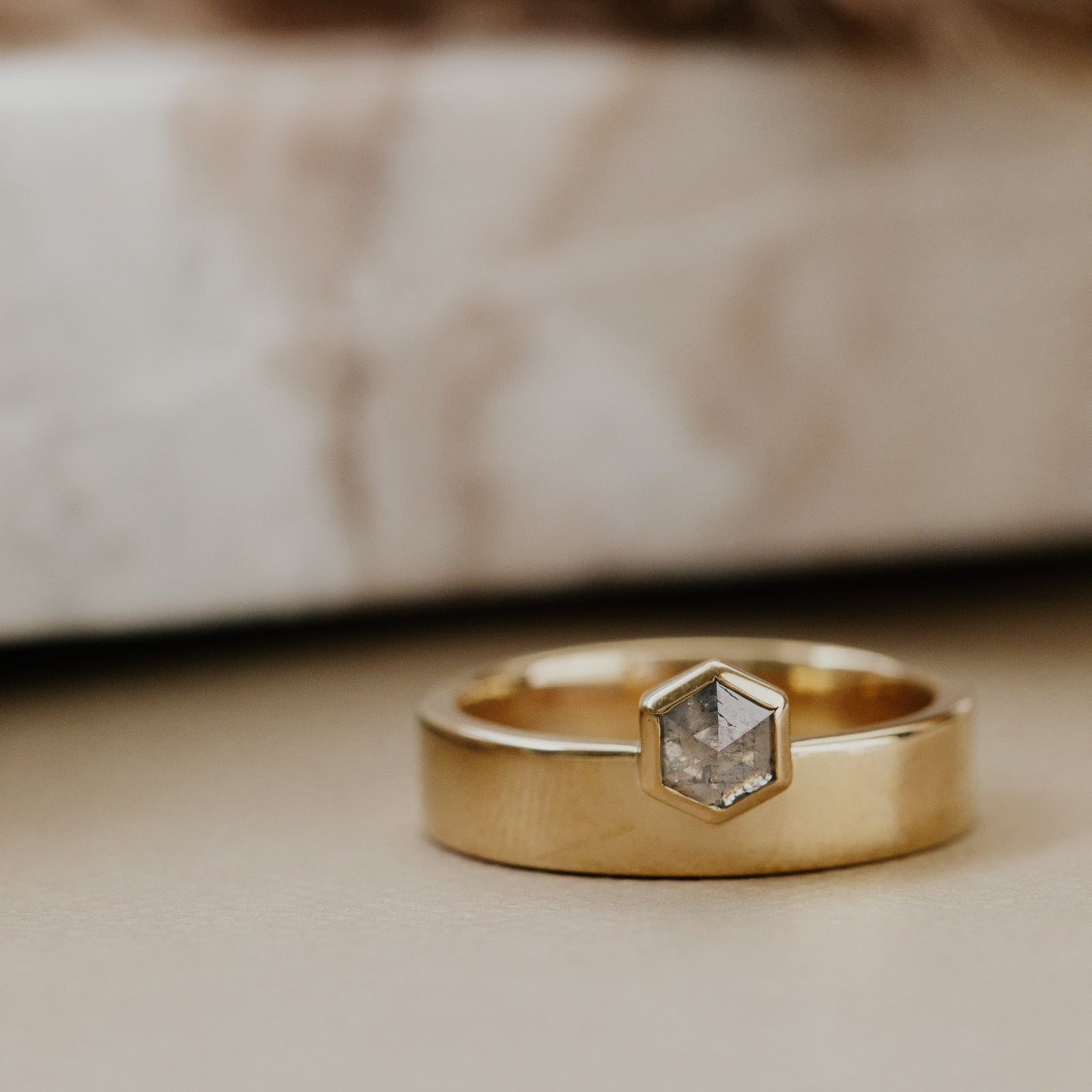 Gold ring with hexagon gray rustic diamond on a soft, blurred background.