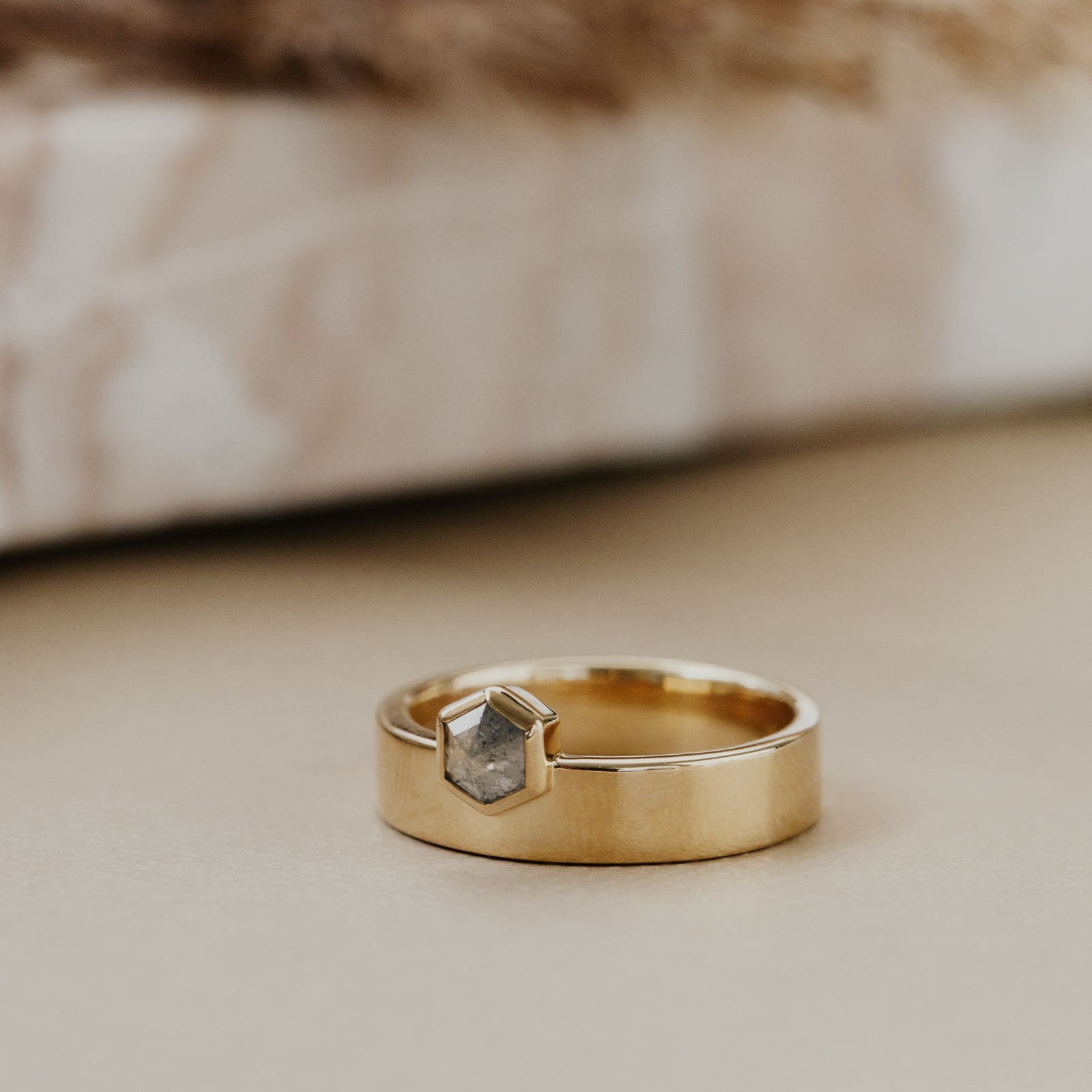 Gold ring with a gray hexagon rustic diamond on a neutral background.