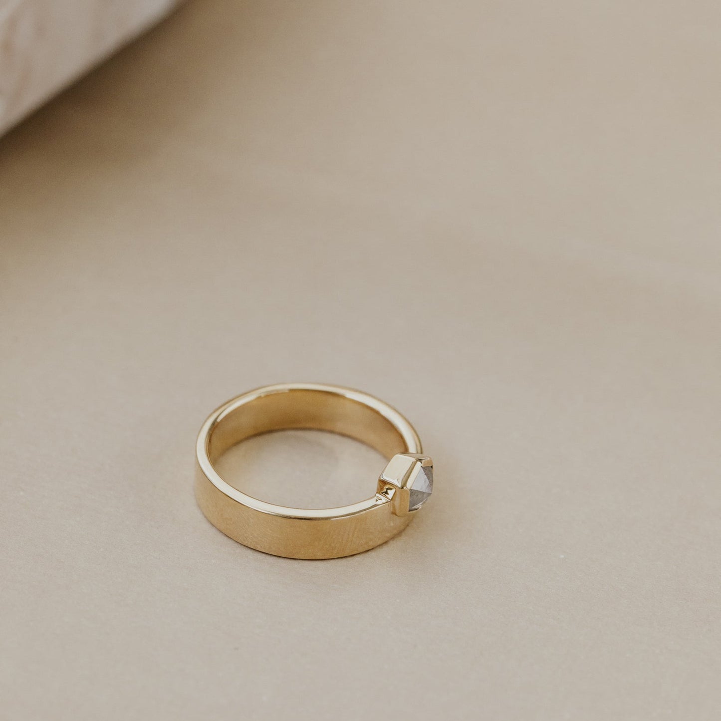 Gold ring with a gray hexagon rustic diamond on a beige surface.