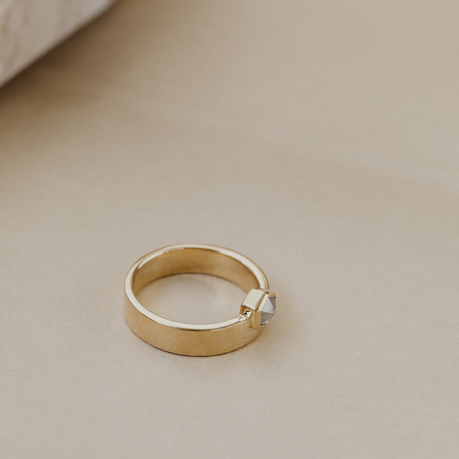 Gold ring with a gray hexagon rustic diamond on a beige surface.