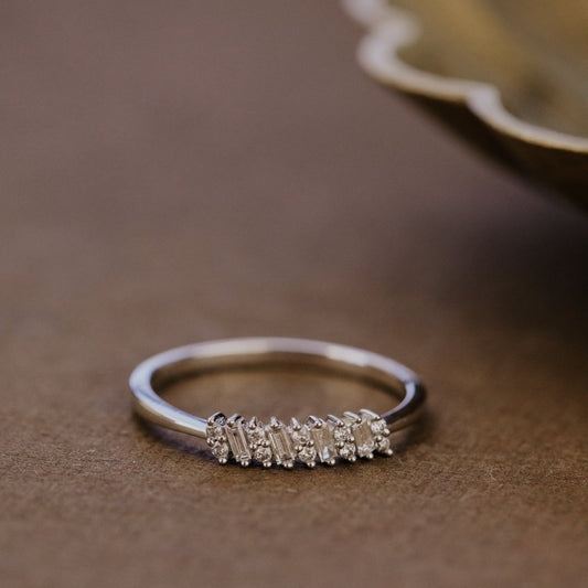 White gold wedding band with diamond accents on a brown surface.