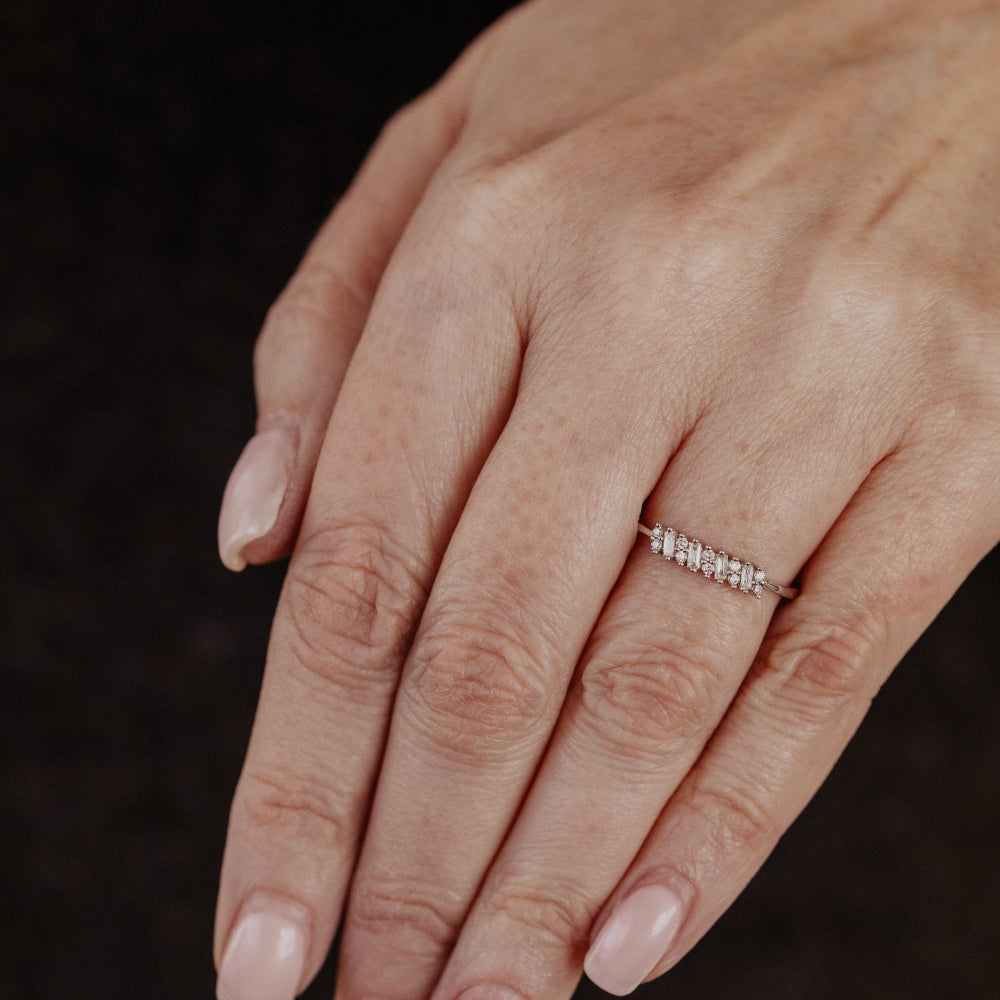 Hand wearing a white gold diamond wedding band on a dark background.