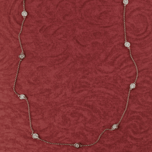 14k gold station bezel, lab grown diamond chain necklace showcased on a textured red surface. 