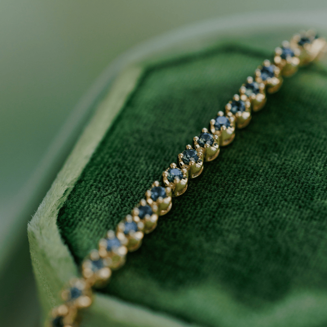 An arial shot of a teal sapphire tennis bracelet on a white background. 