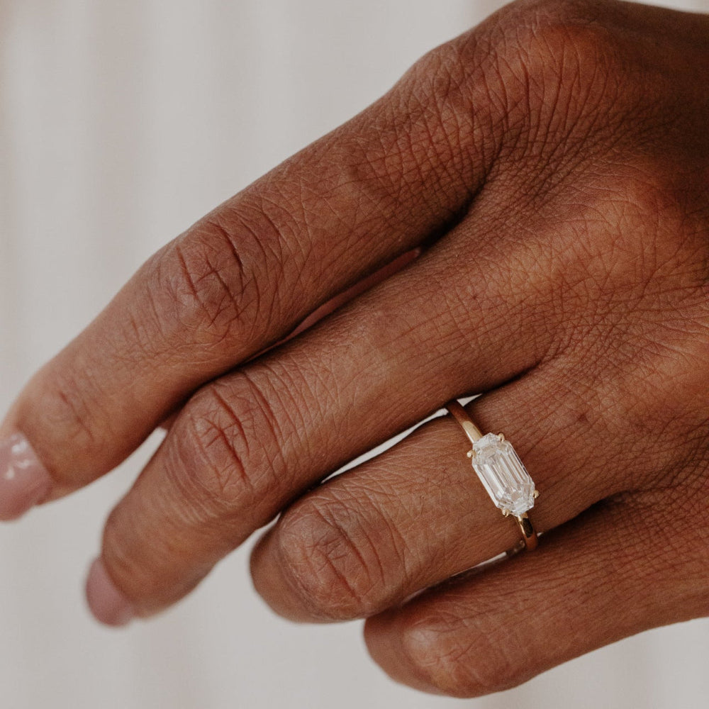 Hand wearing a ring with a lab grown diamond on a neutral background.