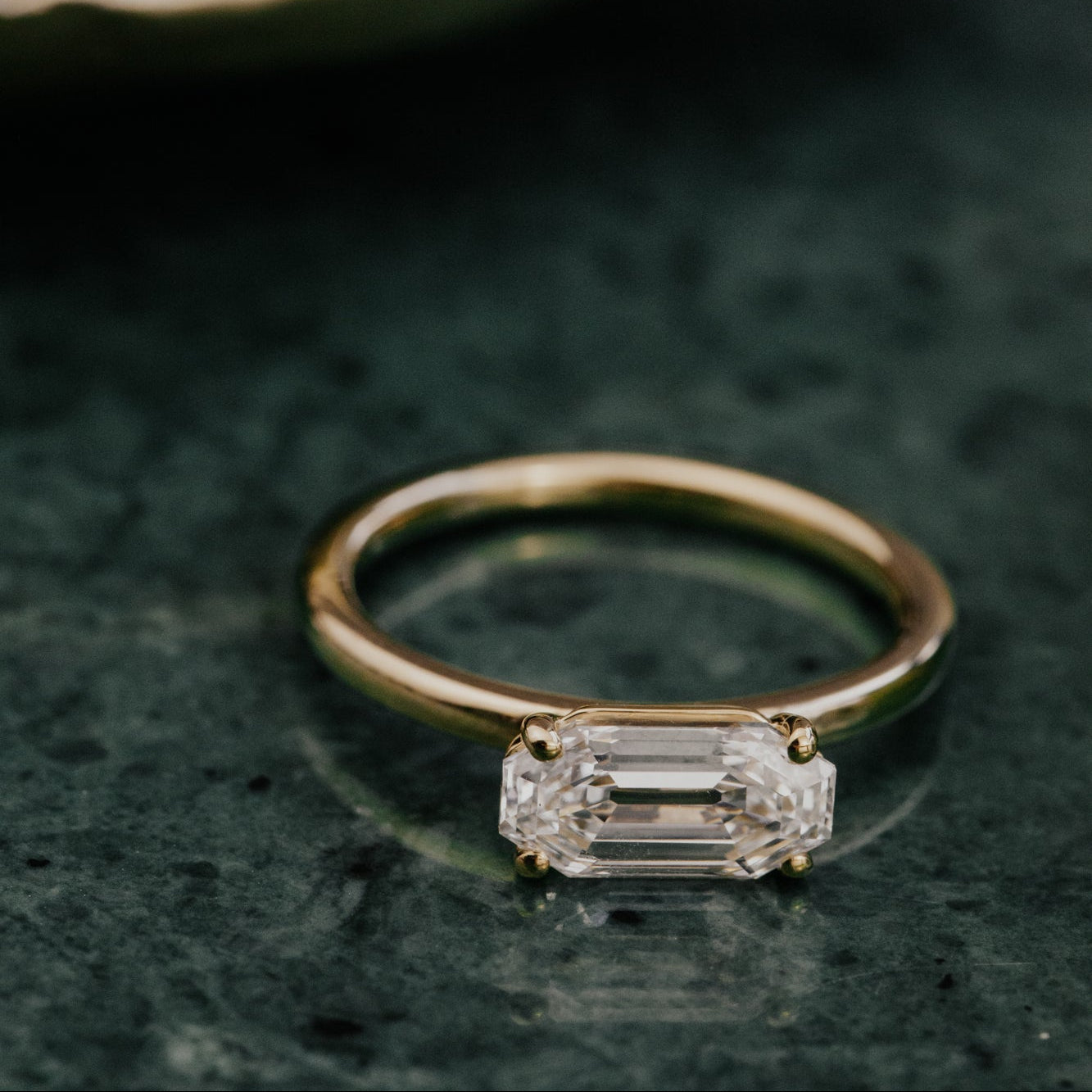 Gold ring with a lab grown diamond on a dark green surface.