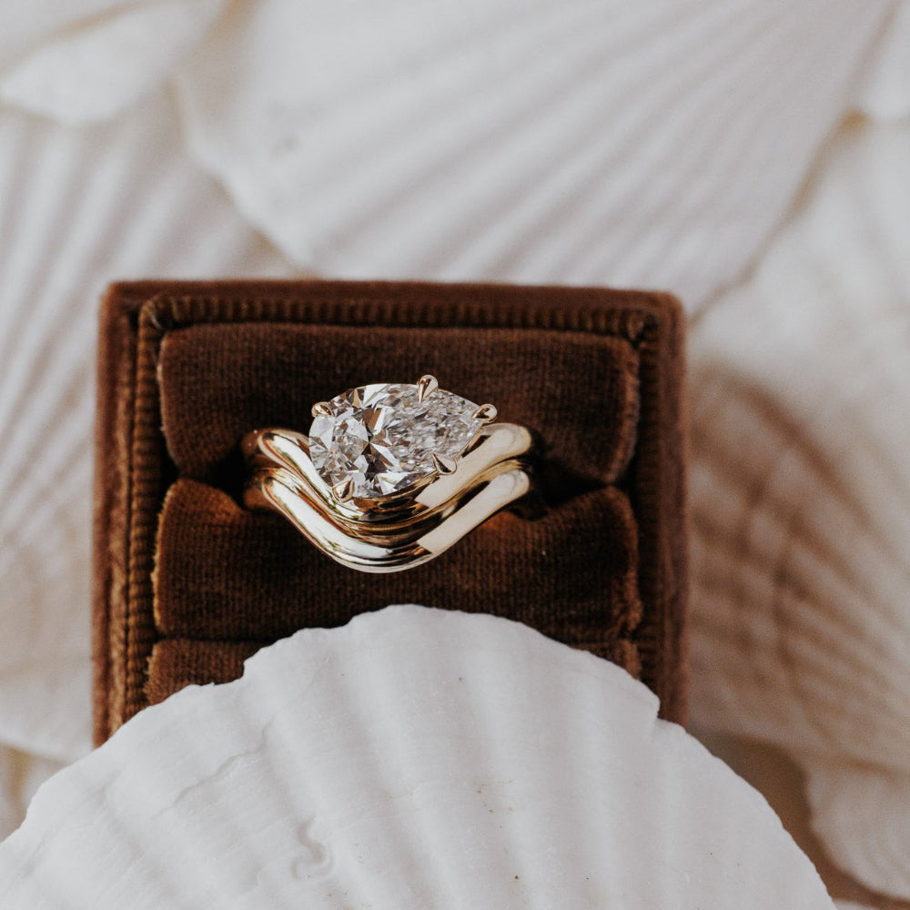 The Capri Pear Ring in 14k yellow gold featuring a lab-grown pear diamond prong set on a double wavy band, displayed in a brown velvet ring box. This 14k gold ring features a pear diamond center stone set in prongs on a double wavy band. This ring is made-to-order based on the selected customizations.