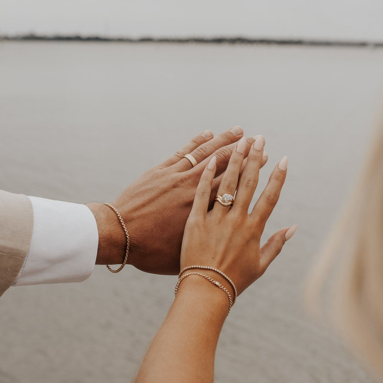 The Capri Pear Ring in 14k yellow gold featuring a lab-grown pear diamond prong set on a double wavy band, worn on the ring finger alongside stacked gold bracelets.