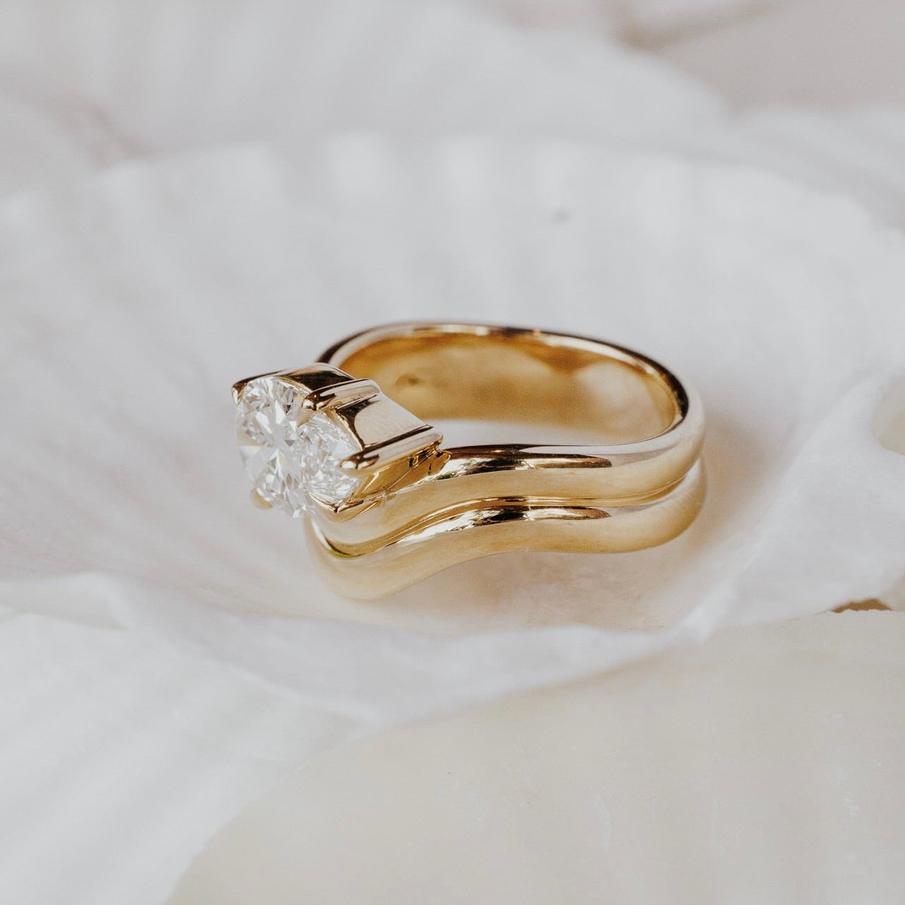 The Capri Pear Ring in 14k yellow gold featuring a lab-grown pear diamond prong set on a double wavy band, shown in profile on white seashell to display the double wavy band structure.