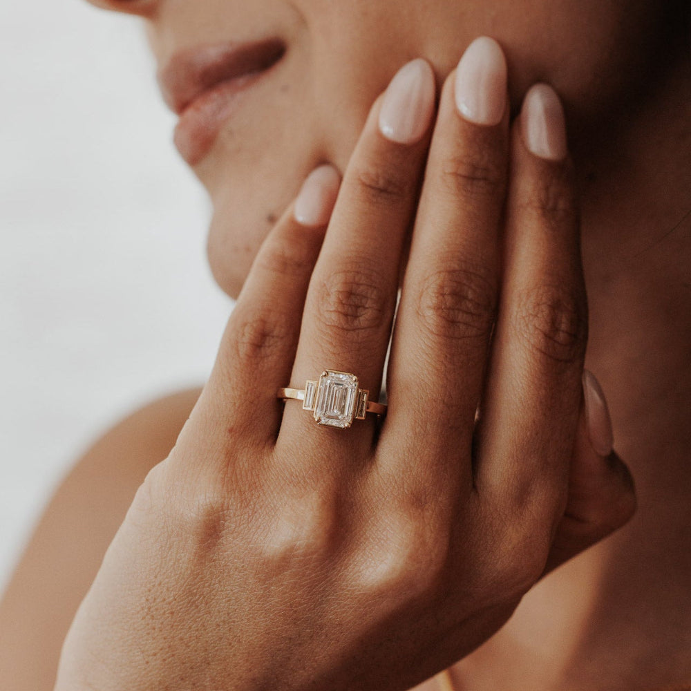 The Carson Emerald Cut Ring in 14k yellow gold featuring an emerald cut center stone with baguette diamond side stones, worn on the ring finger.
