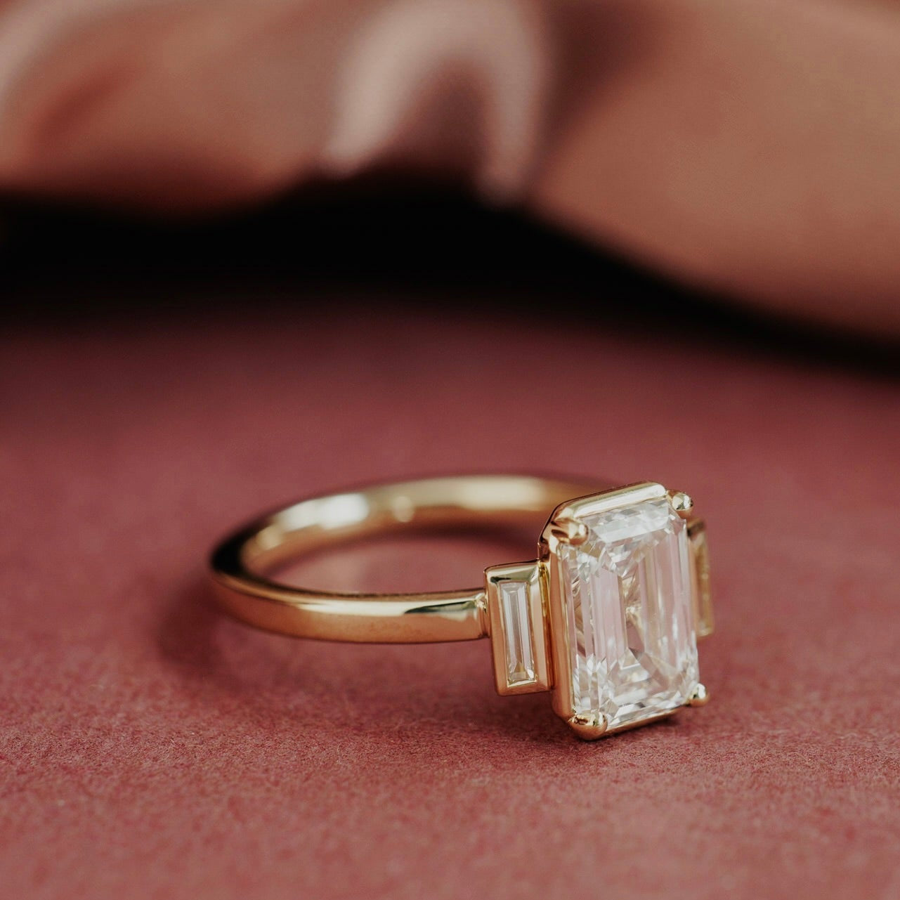 The Carson Emerald Cut Ring in 14k yellow gold featuring an emerald cut center stone with baguette diamond side stones, shown at an angle to display the setting height and band profile.

