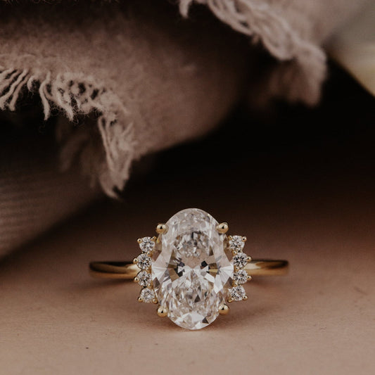 The Claire Oval Ring in 14k yellow gold featuring a lab grown diamond oval center stone set in four prongs with starburst-style side diamonds on a high polish band.