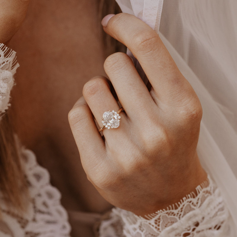 The Claire Oval Ring in 14k yellow gold worn on a bride's hand, showcasing a lab grown diamond oval center stone with starburst-set side diamonds on a slim high polish band.