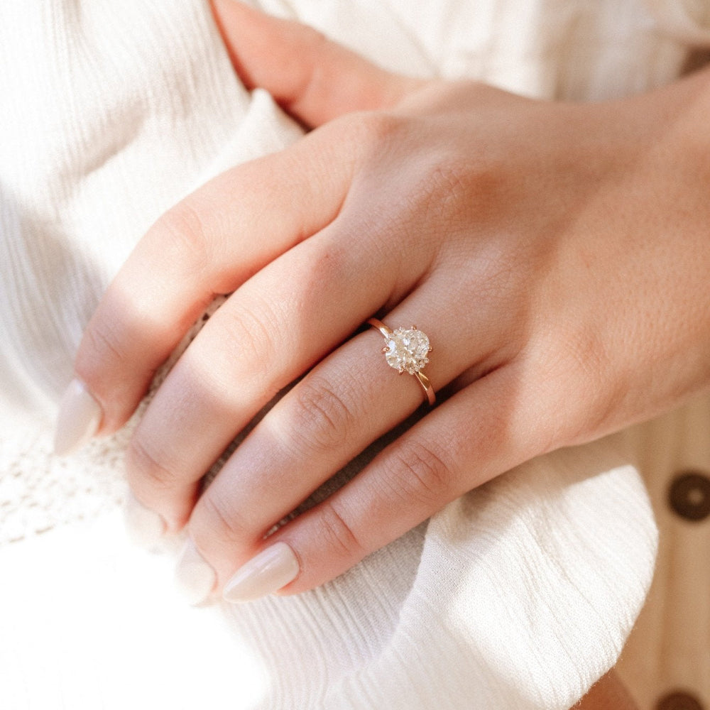 The Claire Oval Ring in 14k rose gold with a lab grown diamond oval center stone on a delicate high polish band, worn on a hand against a soft white background.