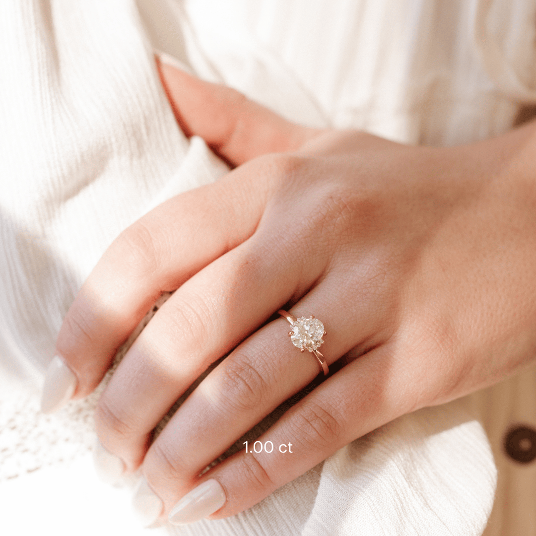 The Claire Oval Ring in 14k rose gold with a lab grown diamond oval center stone on a delicate high polish band, worn on a hand against a soft white background.