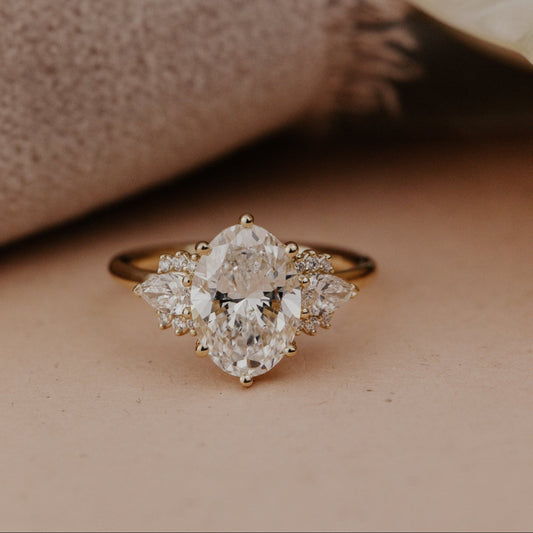 The Daphne Oval Ring in 14k yellow gold featuring a lab grown diamond oval center stone set in six prongs, flanked by pear and round diamond clusters on a high polish band.