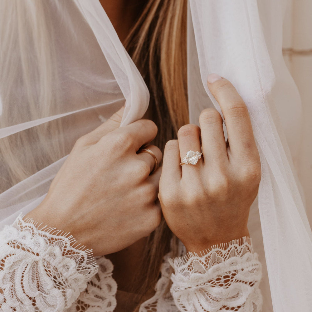 The Daphne Oval Ring in 14k yellow gold with a lab grown diamond oval center stone and pear and round diamond clusters, worn on a bride's hand as she holds a white veil.
