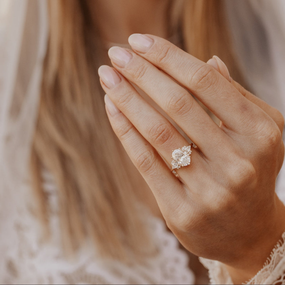 The Daphne Oval Ring in 14k yellow gold featuring a lab grown diamond oval center stone with pear and round diamond clusters, worn on a model's hand.