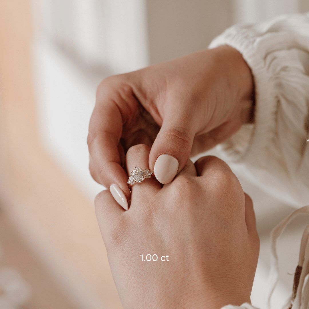 The Daphne Oval Ring in 14k yellow gold with a lab grown diamond oval center stone and pear and round diamond clusters, worn on a hand against a white textured background.
