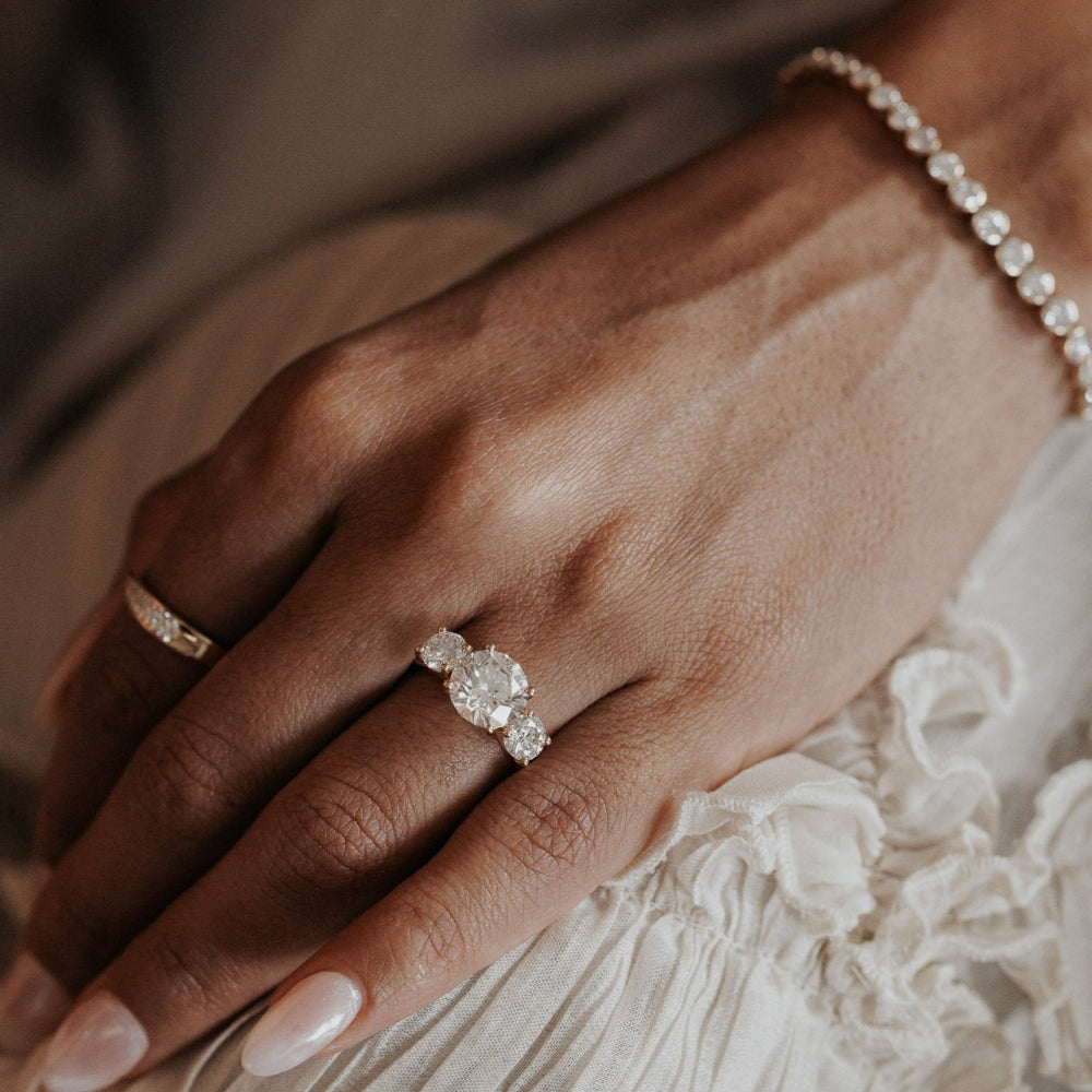 The Hannah Round Ring in 14k yellow gold worn on the ring finger, styled with a diamond eternity band and a diamond tennis bracelet.
