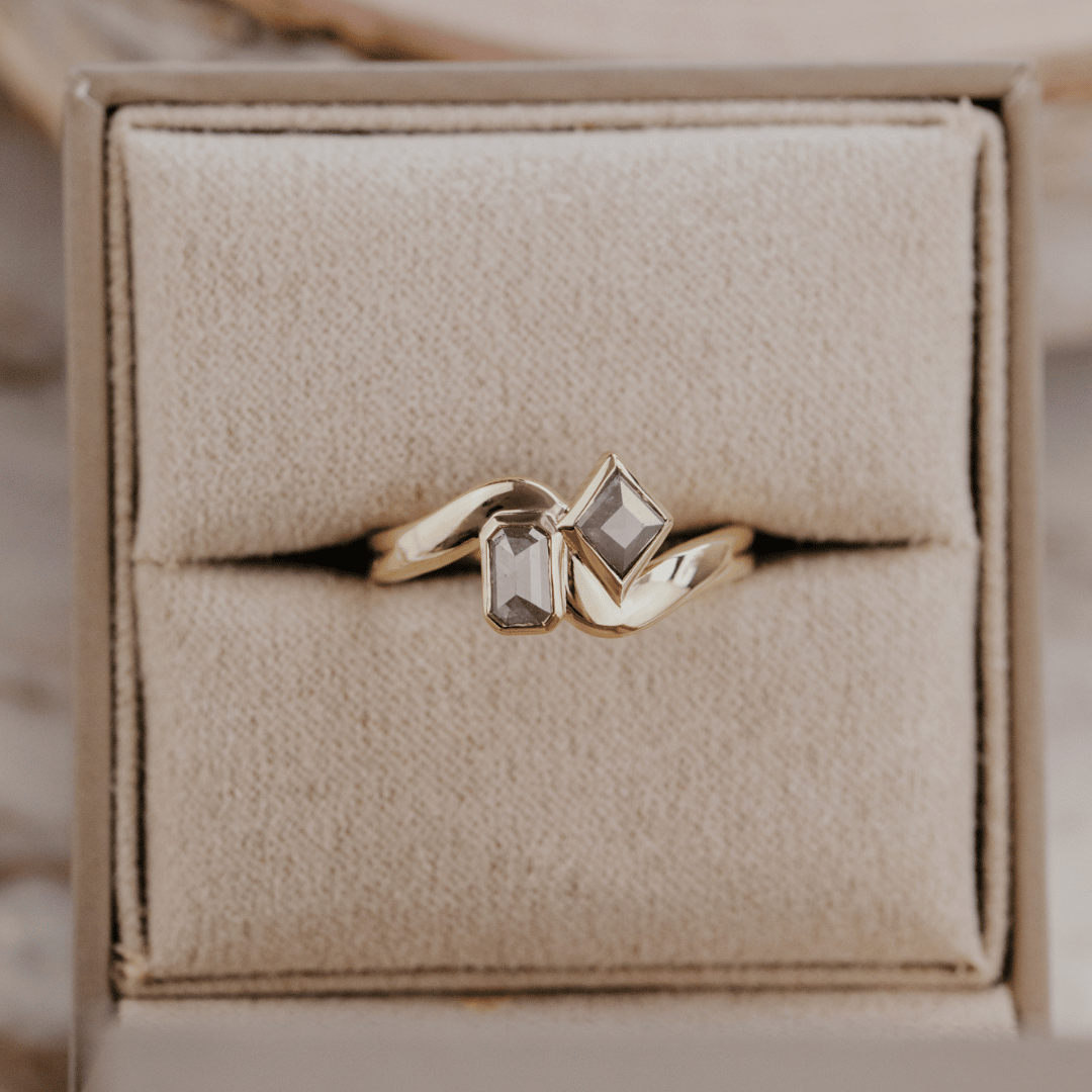 A gold ring with two rustic diamonds displayed in a beige jewelry box.