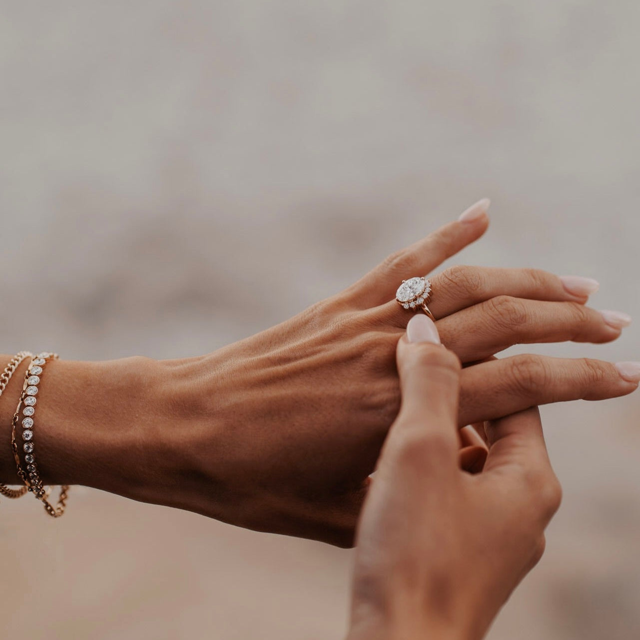The Horizon Oval Ring in 14k yellow gold featuring a lab-grown oval diamond center stone with a round tapered diamond half halo, being placed on the ring finger alongside stacked gold and diamond bracelets.