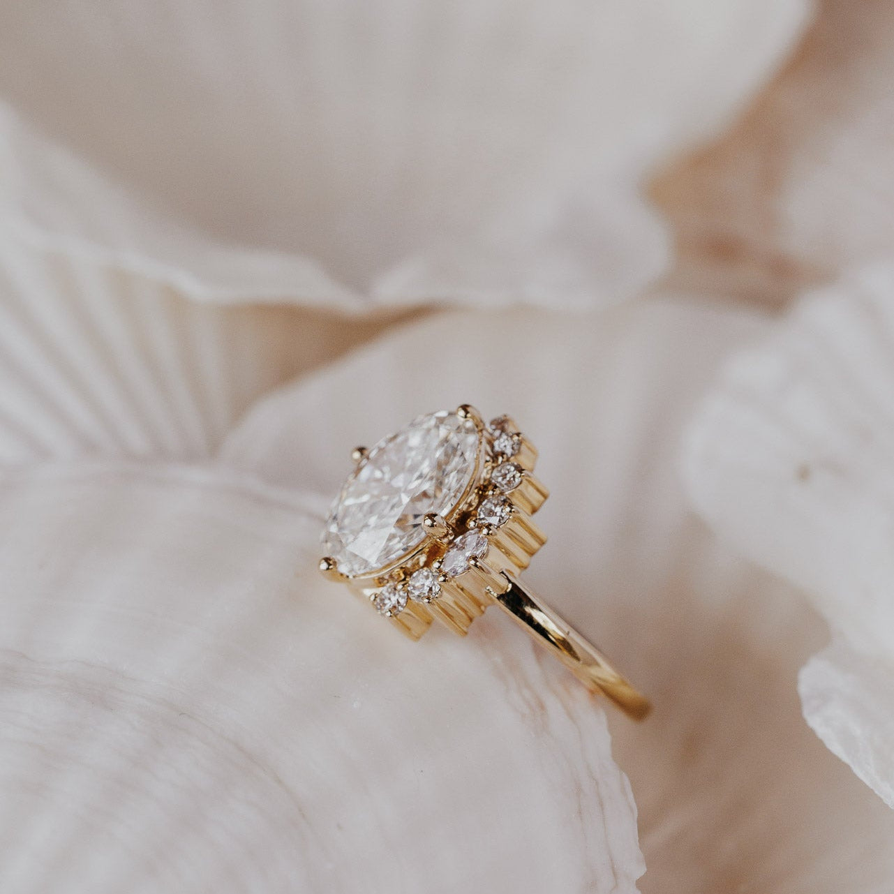 The Horizon Oval Ring in 14k yellow gold featuring a lab-grown oval diamond center stone with a round tapered diamond half halo, displayed on a white shell to show the side profile of the half halo.