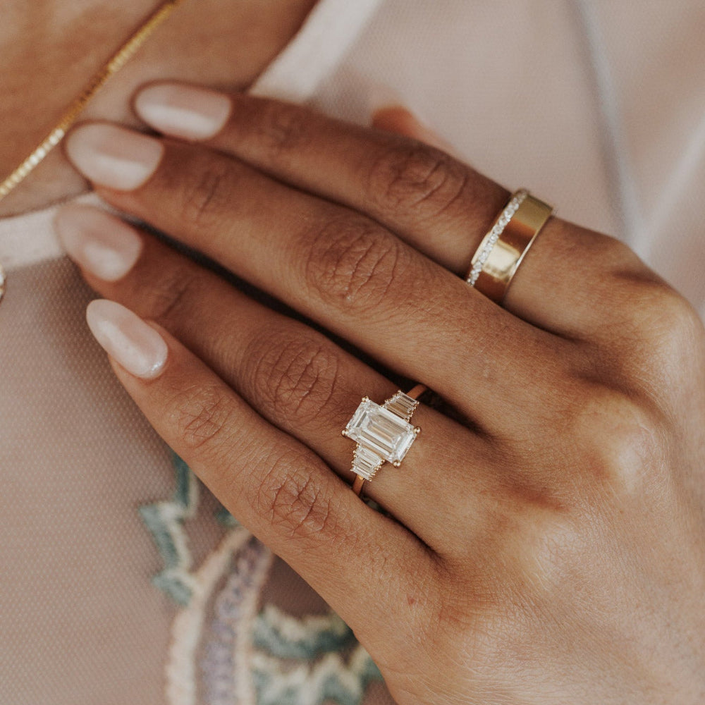 The Jolee Emerald Cut Ring in 14k yellow gold worn on the ring finger, styled with a wide gold band on the middle finger.
