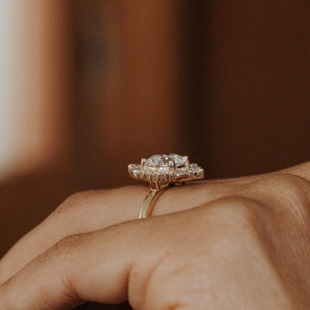 The Lori Round Ring in 14k yellow gold worn on the ring finger, shown from a side profile angle highlighting the ornate diamond halo setting against a warm neutral background.
