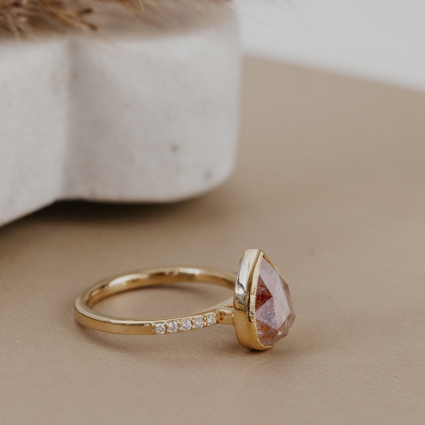 The Lyell 3.24 ct Pear Clear and Peach Rustic Diamond Ring in 14k yellow gold featuring a pear-shaped rose cut rustic diamond in a milgrain bezel with pave diamond band, shown at an angle to display the setting height and pave band detail.
