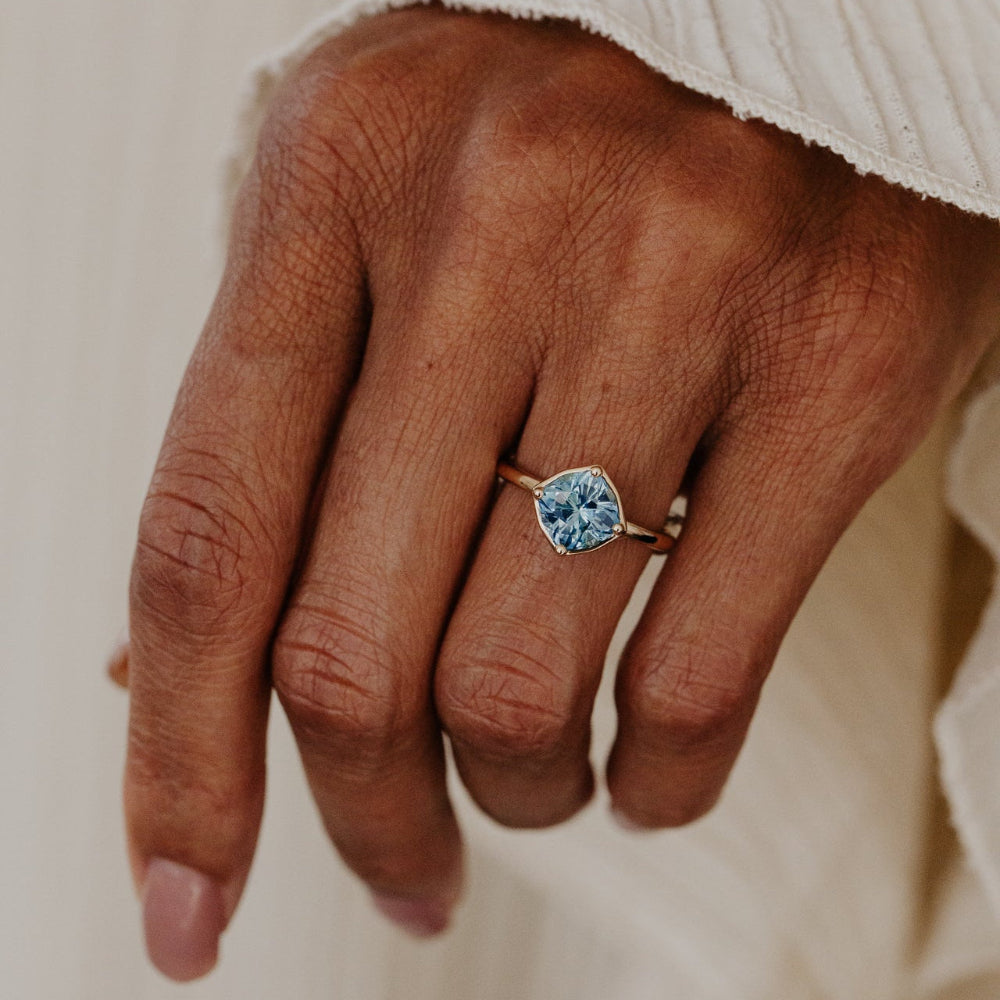 The Maren 2.55 ct Cushion Montana Sapphire Ring in 14k yellow gold featuring a cushion cut Montana sapphire center stone set in four prongs with a high polish gold halo, worn on the ring finger.
