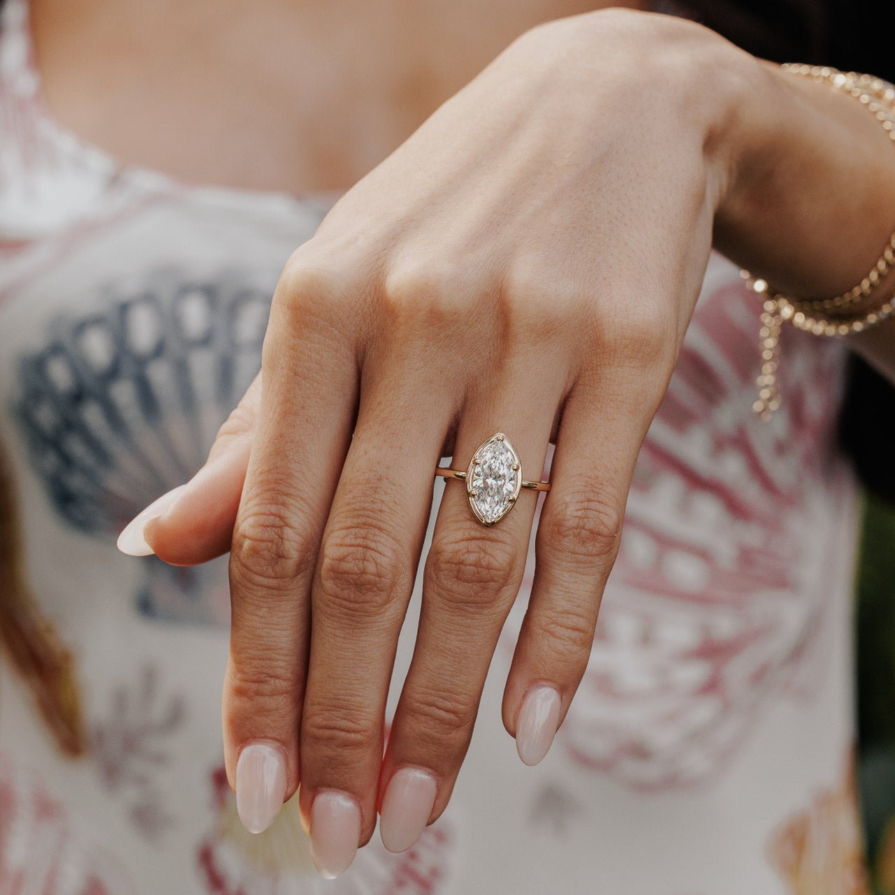 The Maren Ring in 14k yellow gold featuring a lab-grown marquise diamond center stone set with six prongs in a high polish gold halo, worn on the ring finger alongside stacked gold bracelets.